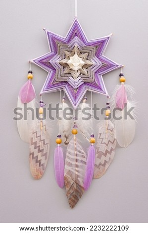 Handmade esoteric woven mandala magical dreamcatcher with feathers and amethyst gemstone on grey background, meditation tool for yoga room interior