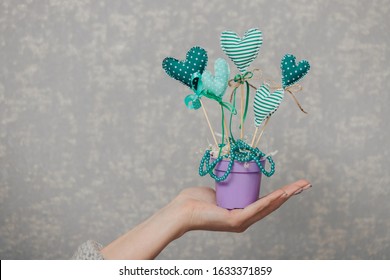 Handmade fabric hearts on sticks in a pot. The girl holds a handicraft in hand on a gray background. - Powered by Shutterstock