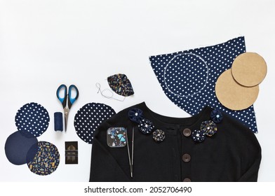 Handmade fabric yo-yo flowers are used to decorate women's black cashmere sweater. Round shreds of silk with polka dots, scissors, needles, threads and beads nearby on a white background. DIY concept