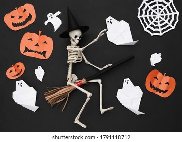 Handmade Halloween paper cut decor and skeleton on broomstick. Black background. Halloween background. Top view. Flat lay - Powered by Shutterstock