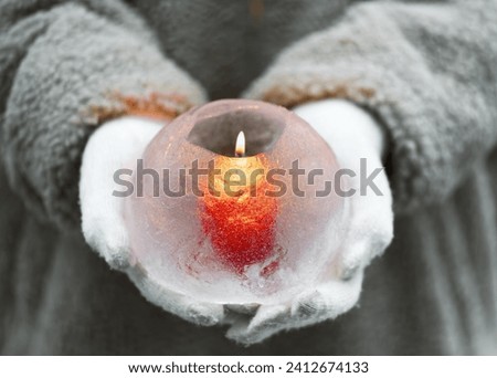 Handmade ice globe lantern with red candle burning in the girls hands. Winter craft and Ice art or outdoor decoration concept.
