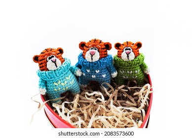 Handmade Knitted Soft Toy. Amigurumi. There Are Three Toy   Tigers Sit  In  The Box On The White Background. Crochet And Knitting  Stuffed Animals. Group Of Small Toys