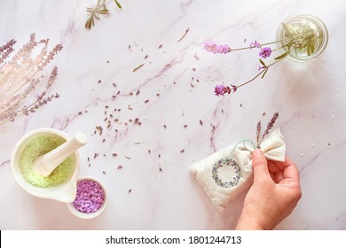 Handmade Lavender Sachets And Home Made Sugar Scrub. Hand Holds Linen Bag With Dry Lavender Flowers. Top View On White Marble Table.