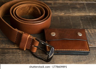 Handmade leather wallet and belt in cognac brown color on a wooden table. Vintage leather wallet and belt. Handmade leather goods. Leather craft.