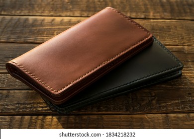 Handmade leather wallets in brown and black on a wooden table.