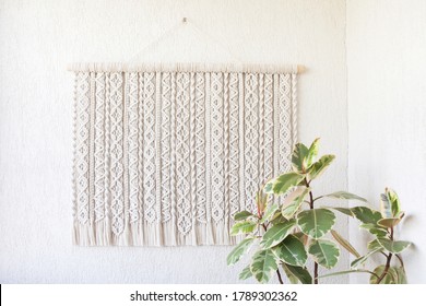 Handmade macrame. 100% cotton wall decoration with wooden stick hanging on a white wall. Female hobby. ECO friendly modern knitting DIY natural decoration concept in the interior