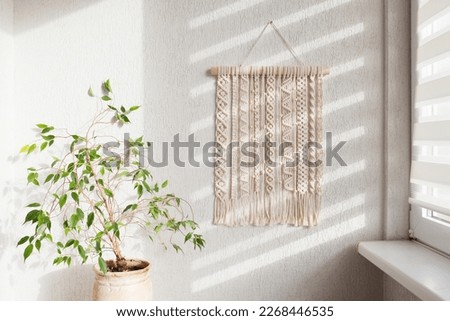 Handmade macrame. 100% cotton wall decoration with wooden stick hanging on a white wall. Macrame braiding and cotton threads. Female hobby. ECO friendly modern knitting  natural decoration in interior