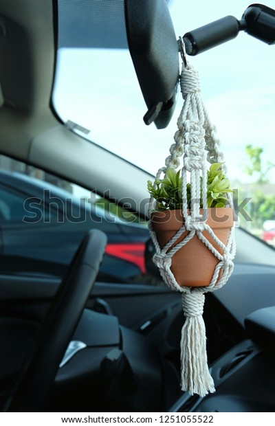 A hand-made mini macrame\
plant hanger made out of 100 percent cotton, holding a ceramic pot\
with a faux (fake) plant inside. The macrame is a car accessory\
decoration.