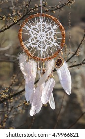 Handmade native americans dream catcher with white doily on background of spring branches. Tribal elements, feathers, lace, crochet snowflake
