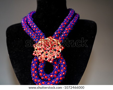 Handmade necklace made of red and blue beads with a golden brooch and matching earrings on a black mannequin