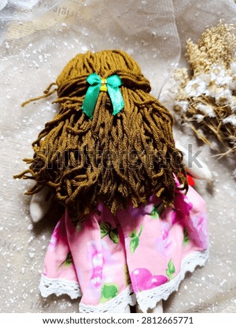 Handmade Rag Doll Back View Brown Hair Green Bow
Description: Back view of a handmade fabric doll with brown yarn hair tied with a green ribbon bow, wearing a pink floral dress with lace trim.
