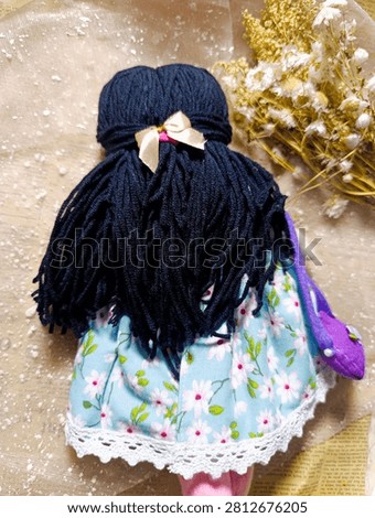 Handmade Rag Doll Back View Dark Hair Blue Dress
Description: Back view of a handmade fabric doll with dark navy yarn hair, wearing a light blue floral dress with a purple accessory detail.
