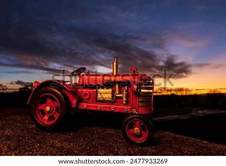 Handmade scale model of a red tractor with a morning sky in the background.