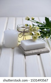 Handmade soap with a pattern lies on the table.  On a white table is handmade soap, flowers and olive oil.  Collection of items for the bathroom