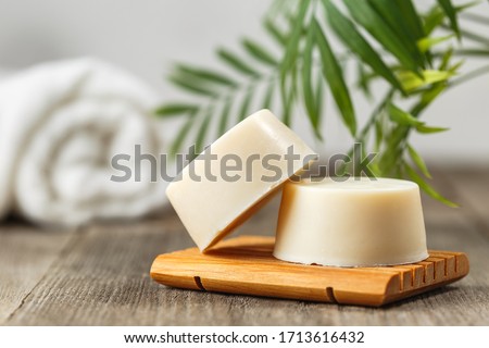 Handmade solid shampoo soap bar on wooden dish. Green leaves above and towel on the background. Zero waste, eco friendly product