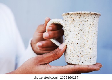 Handmade speckled ceramic mug held by African American woman against a gray background outside by the handle - Powered by Shutterstock