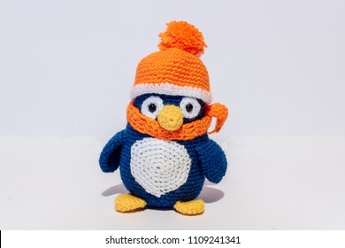 Handmade stuffed toy penguin, in orange hat, on white background, horizontal.