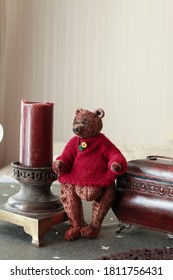 Handmade Teddy Bear In Vintage Style, Purpously Aged, Red Knited Sweater. Decoration, Wooden Box And Ancient Candleholder Next To The Toy. Concept Of Nostalgic Childhood  Memories From The Past