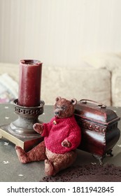 Handmade Teddy Bear In Vintage Style, Purpously Aged, Red Knited Sweater. Decoration, Wooden Box And Ancient Candleholder Next To The Toy. Concept Of Nostalgic Childhood  Memories From The Past