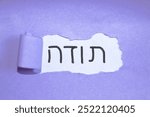 Handmade thank you expression in Hebrew “תודה” written on white paper with purple background. Concept of courtesy and respect.