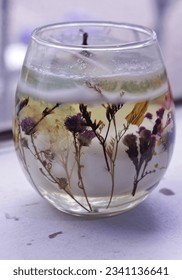 Handmade transpa candle in a glass cup decorated with dried leaves and flowers.