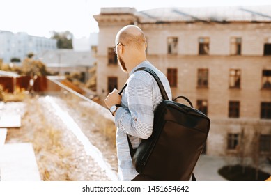 Handome guy with stylish backpack, looking away, ans standing on  terrace, blurry building background