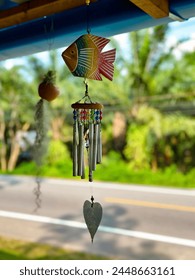 A hand-painted fish wind chime with metal tubes and beads hanging outdoors, a whimsical addition to garden decor