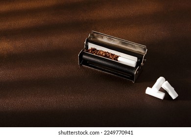 Hand-rolled cigarette, rolling machine, scattered tobacco on background, cigarette roll with filter, cigarette filters
