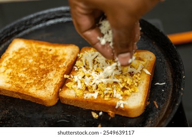 Hands adding cheese to scrambled eggs on toast in a frying pan. Quick and easy breakfast or snack. - Powered by Shutterstock