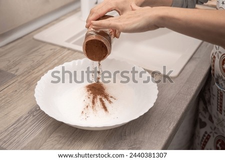 Hands adding ground cinnamon to sugar in a white bowl for dessert preparation.