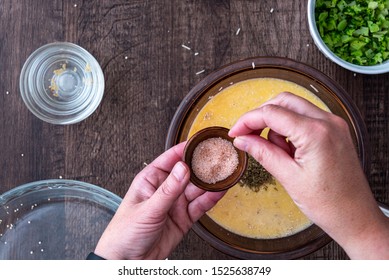 Woman’s hands adding a pinch of pink Himalayan salt to raw egg mixture in glass bowl, on a wood table
 - Powered by Shutterstock