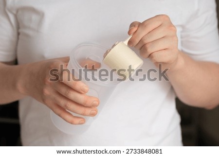 Hands adding protein powder into a shaker bottle. Sports nutrition, fitness preparation and workout routine concept. Close-up of scoop and reusable container.