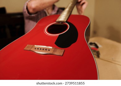 Hands adjusting and changing strings on a red acoustic guitar, illustrating guitar maintenance, repair and setup for improved playability.