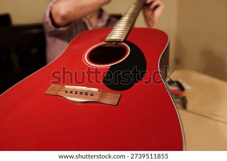 Hands adjusting and changing strings on a red acoustic guitar, illustrating guitar maintenance, repair and setup for improved playability.
