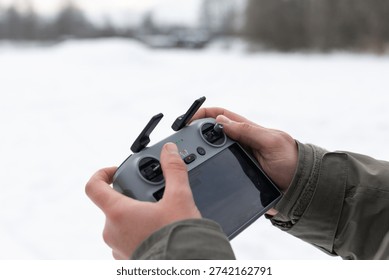 Hands adjusting a compact drone controller with built-in display against a bright snowy backdrop. Green status lights and tactile sticks emphasize user interaction and intuitive, responsive flight controls.