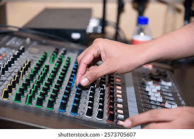 Hands adjusting the knobs and faders on a professional audio mixing console in a studio