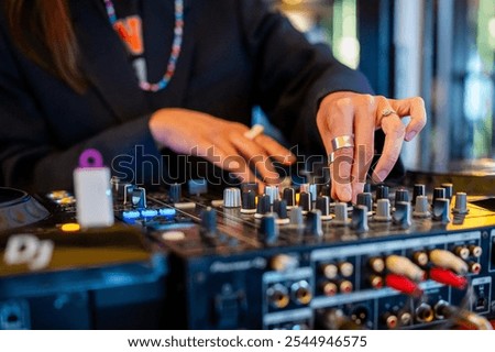 A DJ’s hands adjusting knobs on a mixer, vibrant nightlife scene with focus on music control. Perfect for themes of music, nightlife, entertainment, and DJing