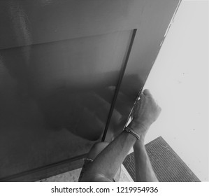 Hands Affixing Adhesive Rubber Draft Proofing To A Door Frame. In Monochrome