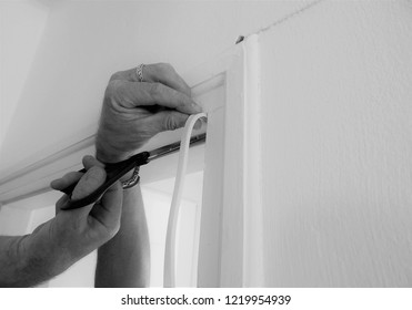 Hands Affixing Adhesive Rubber Draft Proofing To A Door Frame. In Monochrome