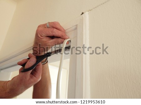 hands affixing adhesive rubber draft proofing to a door frame.