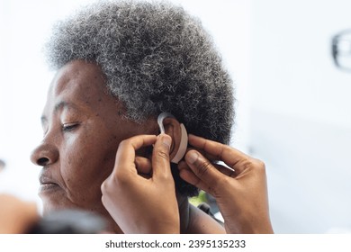 Hands of african american female doctor applying hearing aid to senior woman in hospital room. Medicine, healthcare and medical services, unaltered. - Powered by Shutterstock