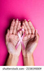 Hands of african american mid adult woman holding pink breast cancer awareness ribbon, copy space. pink background, breast, cancer, medical, awareness, support, healthcare and alertness concept. - Shutterstock ID 2158190009