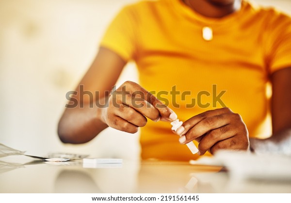 Hands of African female with HIV and Aids at\
home blood self test kit sitting at a desk waiting to check for\
results. Closeup of young afro woman with medicine or pills for a\
medical condition.
