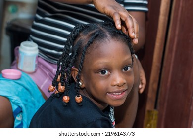 Hands of an african hair stylist or mother making braided hairstyle on the head of a little girl child at a saloon