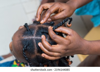 Hands Of An African Hair Stylist Or Mother Making Braided Hairstyle On The Head Of A Little Girl Child At A Saloon