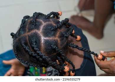 Hands Of An African Hair Stylist Or Mother Making Braided Hairstyle On The Head Of A Little Girl Child At A Saloon