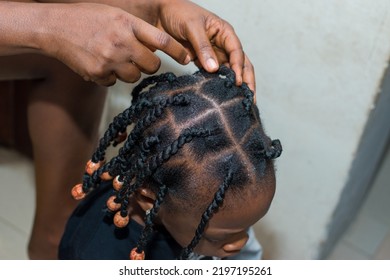 Hands Of An African Hair Stylist Or Mother Making Braided Hairstyle On The Head Of A Little Girl Child At A Saloon