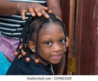 Hands Of An African Hair Stylist Or Mother Making Braided Hairstyle On The Head Of A Little Girl Child At A Saloon