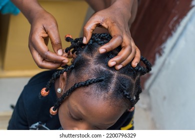 Hands Of An African Hair Stylist Or Mother Making Braided Hairstyle On The Head Of A Little Girl Child At A Saloon