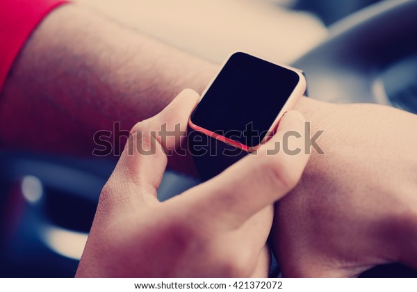 Hands of african male model\
using trendy smart wrist watches in a car. Popular new technology\
to always stay connected to internet and social media. Close up\
macro 